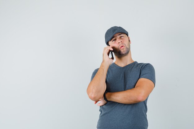 Młody mężczyzna rozmawia przez telefon komórkowy w czapce t-shirt i patrząc niezdecydowany