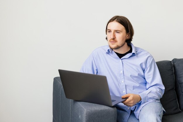 Młody mężczyzna siedzący na kanapie z laptopem
