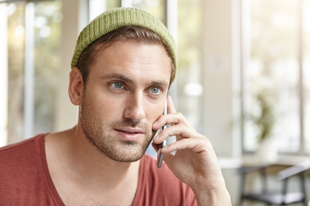 Młody mężczyzna siedzi w kawiarni rozmawia przez telefon