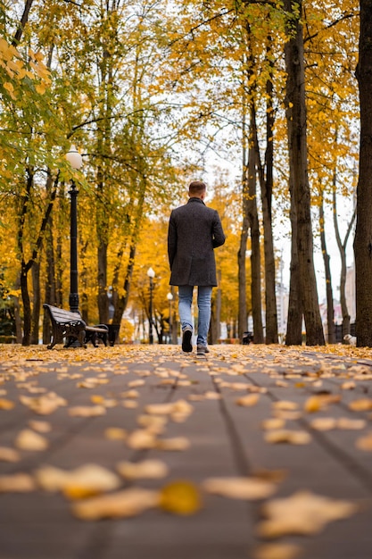 Młody mężczyzna spacerujący po jesiennym mieście ze szklanką kawy