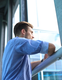 Młody mężczyzna stojący przy oknie w swoim biurze i myślący o swoich celach