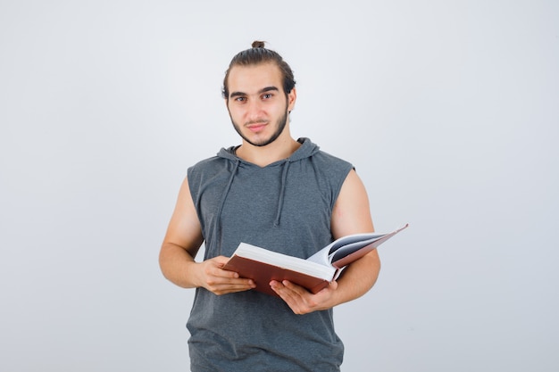 Młody mężczyzna trzyma książkę patrząc na kamery w bluzę bez rękawów z kapturem i patrząc przystojny. przedni widok.