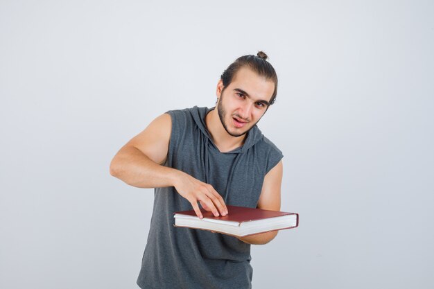 Młody mężczyzna trzyma książkę w bluzie bez rękawów i wygląda pewnie, widok z przodu.