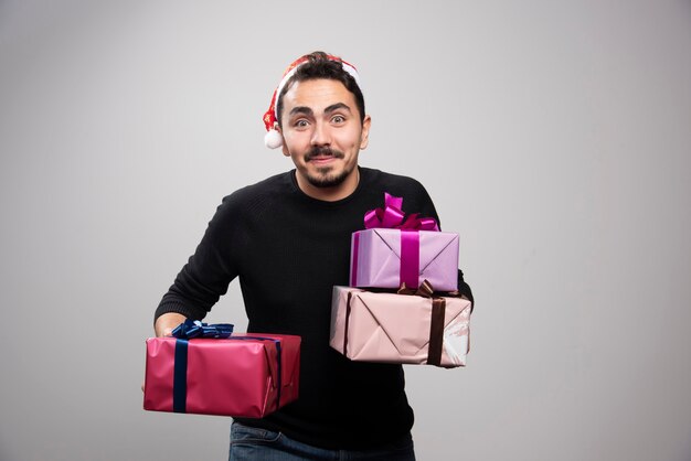 Młody mężczyzna trzyma pudełka na prezenty na szarej ścianie.