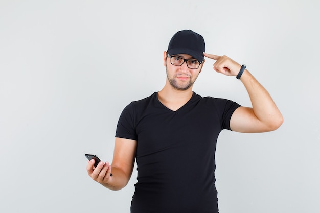 Młody mężczyzna trzyma smartfon, wskazując na głowę w czarnej koszulce