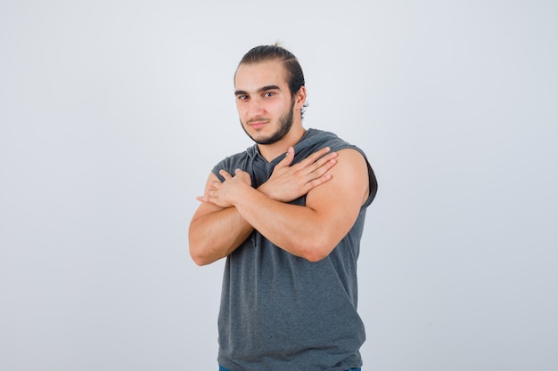 Młody mężczyzna trzymający skrzyżowane ramiona na piersi w bluzie bez rękawów i wyglądający inteligentnie. przedni widok.
