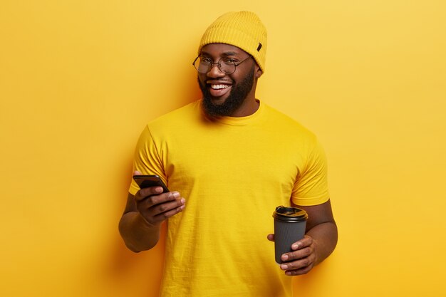 Młody mężczyzna ubrany na żółto trzymając telefon i filiżankę kawy