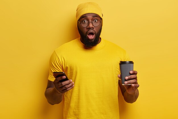 Młody mężczyzna ubrany na żółto trzymając telefon i filiżankę kawy