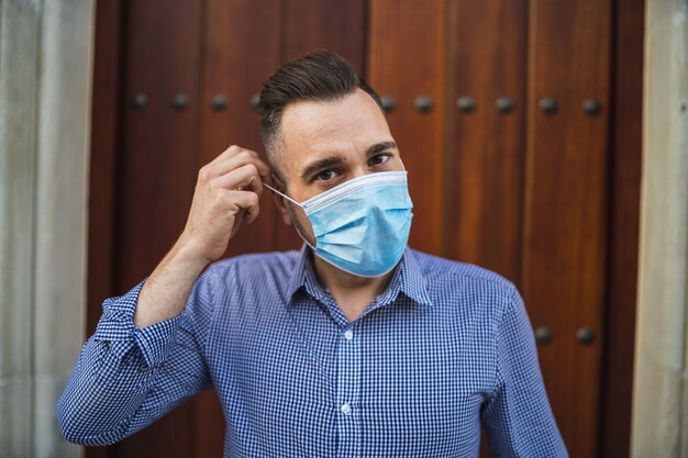 Młody mężczyzna ubrany w niebieską koszulę stojący przy bramie z medyczną maską na twarz