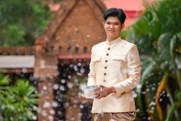 Młody Mężczyzna Ubrany W Piękne Tajskie Kostiumy Delektuje Się Chlapaniem Wodą Z Miski W świątyni I Zachowuje Dobrą Kulturę Tajów Podczas Festiwalu Songkran Podczas Kwietniowego Tajlandzkiego Nowego Roku.