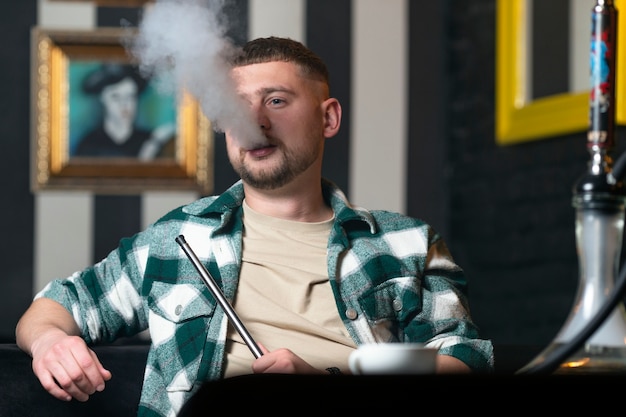 Młody mężczyzna vaping z fajki wodnej w barze