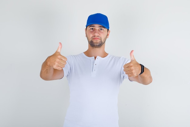 Młody mężczyzna w białej koszulce, niebieskiej czapce pokazującej kciuki do góry i pewnej siebie