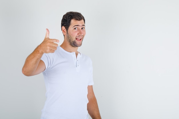 Młody mężczyzna w białej koszulce pokazując kciuk do góry, uśmiechnięty i zadowolony