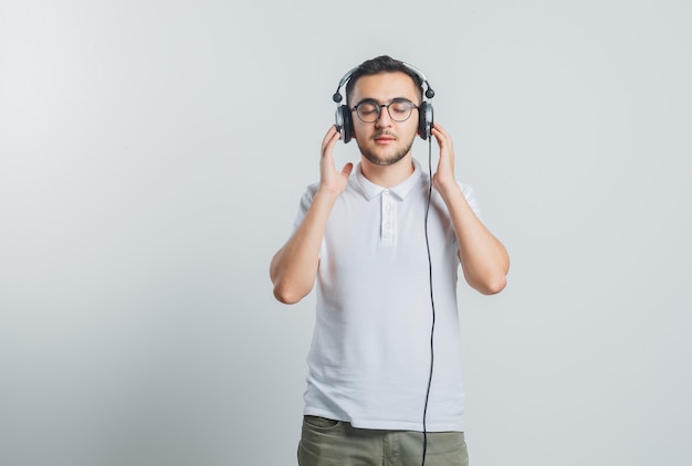 Młody mężczyzna w białej koszulce, spodnie słuchające muzyki w słuchawkach i wyglądający na zrelaksowanego