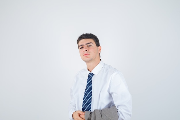 Młody mężczyzna w białej koszuli, krawat trzymający kurtkę na ramieniu podczas pozowania