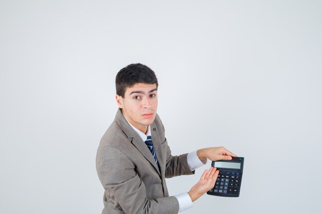 Młody mężczyzna w formalnym garniturze trzymający kalkulator, wskazujący na niego