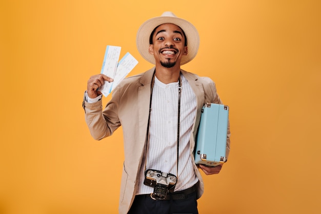 Młody mężczyzna w koszuli i kapeluszu trzymający bilety i walizkę