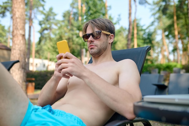 Młody mężczyzna w okularach przeciwsłonecznych ze smartfonem w dłoni