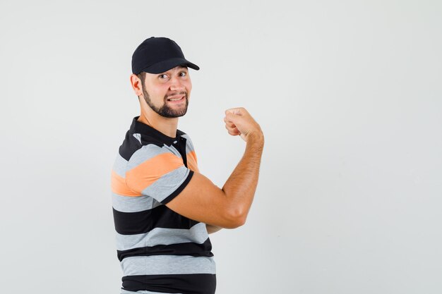 Młody mężczyzna w t-shirt, czapka pokazująca swoje mięśnie i wyglądająca pewnie.
