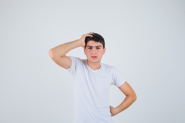 Młody mężczyzna w t-shirt, trzymając rękę na głowie i patrząc zamyślony, widok z przodu.