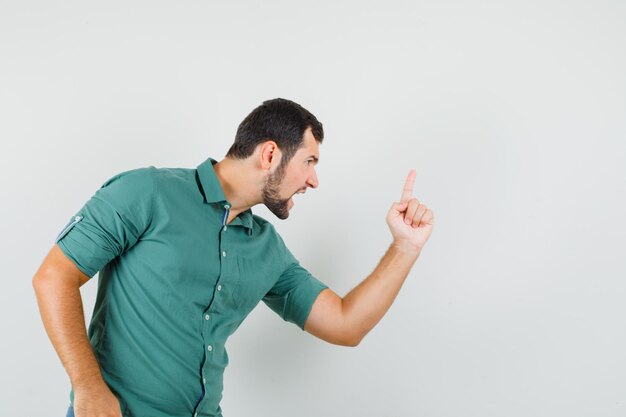 Młody mężczyzna wskazując na bok, krzycząc w sposób agresywny w zielonej koszuli i wyglądając na zły. przedni widok.