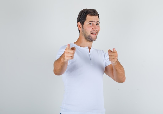 Młody mężczyzna wskazując palcami na aparat w białej koszulce i patrząc wesoło