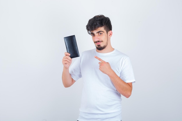 Młody mężczyzna wskazujący na portfel w białej koszulce i wyglądający na pewny siebie