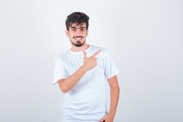 Młody mężczyzna wskazujący na prawy górny bok w koszulce i wyglądający na szczęśliwego