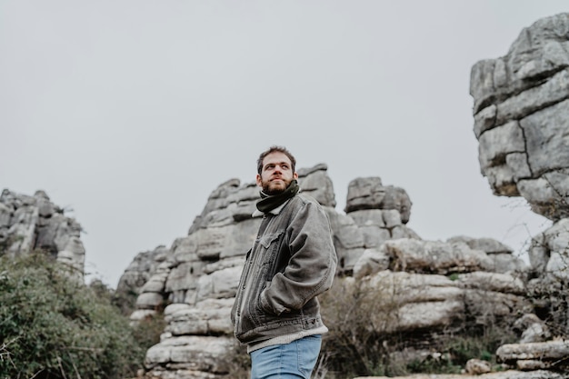 Młody mężczyzna z kurtką stojący w pobliżu skalistych klifów, patrząc na bok