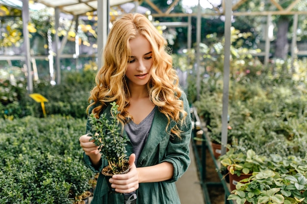 Młody miłośnik flory spaceruje po ogrodzie botanicznym. Śliczna blondynka patrzy na rośliny z zainteresowaniem.