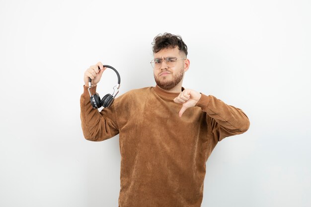 młody model mężczyzna trzyma czarne słuchawki i daje kciuk w dół.