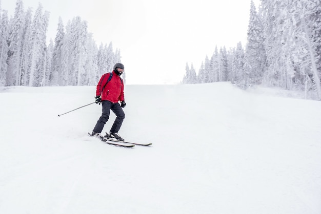 Młody narciarz w ruchu w górskim ośrodku narciarskim z pięknym zimowym krajobrazem