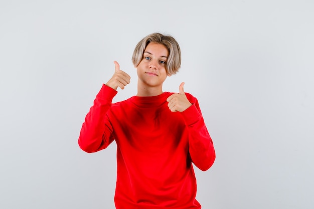 Bezpłatne zdjęcie młody nastolatek w czerwonym swetrze pokazujący podwójne kciuki w górę