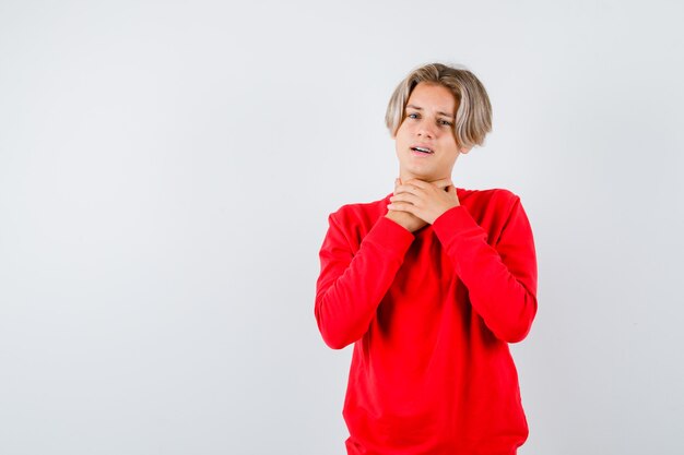 Młody nastoletni chłopak cierpiący na ból gardła w czerwonym swetrze i wyglądający na zaniepokojonego. przedni widok.