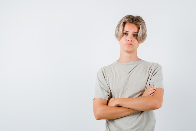 Młody nastoletni chłopak stojący ze skrzyżowanymi rękami w koszulce i wyglądający na rozczarowanego