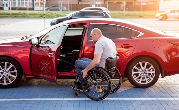 Młody niepełnosprawny kierowca wsiadający do czerwonego samochodu z wózka inwalidzkiego