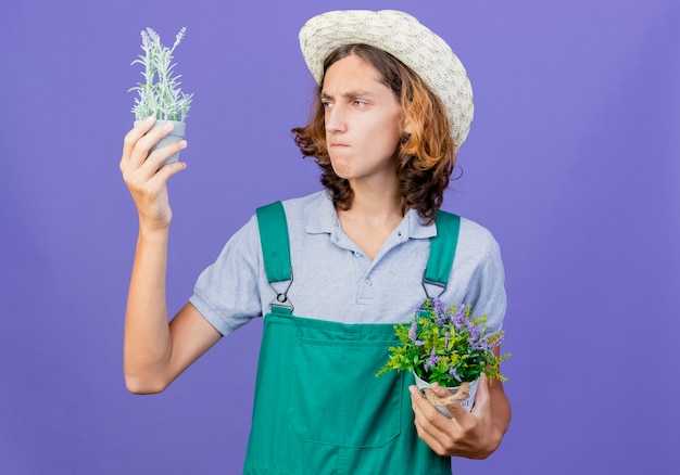 Bezpłatne zdjęcie młody ogrodnik mężczyzna na sobie kombinezon i kapelusz, trzymając rośliny doniczkowe