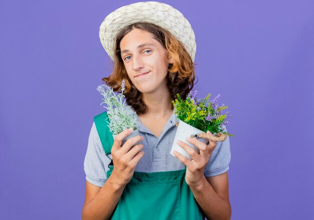 Młody ogrodnik mężczyzna na sobie kombinezon i kapelusz, trzymając rośliny doniczkowe