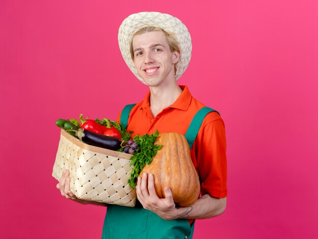 Młody ogrodnik mężczyzna na sobie kombinezon i kapelusz, trzymając skrzynię pełną warzyw