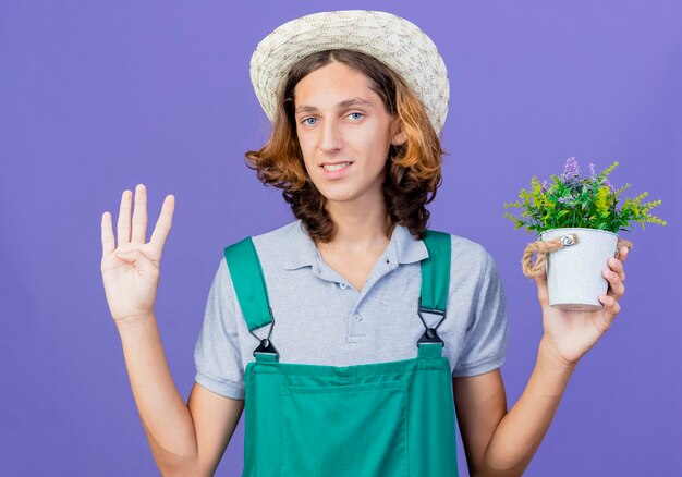 Młody ogrodnik mężczyzna ubrany w kombinezon i kapelusz gospodarstwa doniczkowa roślina z uśmiechem