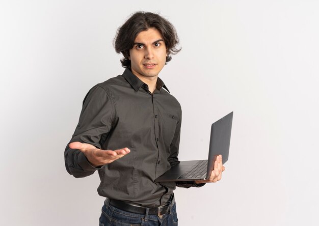Młody pewny siebie przystojny kaukaski mężczyzna trzyma laptopa i wyciąga rękę na białym tle na białym tle z miejsca na kopię