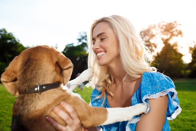Młody piękny blondynki dziewczyny odprowadzenie, bawić się z beagle psem w parku.