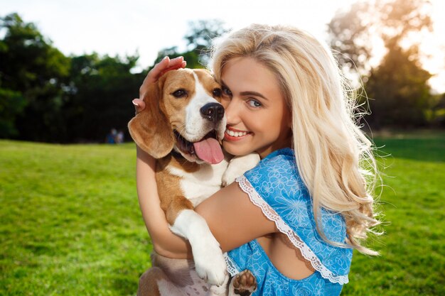 Bezpłatne zdjęcie młody piękny blondynki dziewczyny odprowadzenie, bawić się z beagle psem w parku.