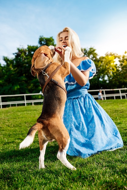 Młody piękny blondynki dziewczyny odprowadzenie, bawić się z beagle psem w parku.