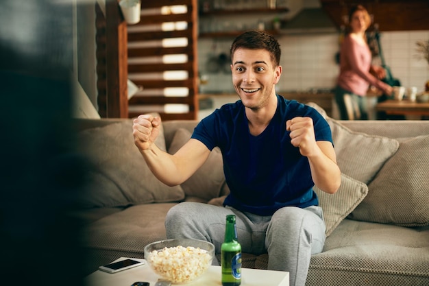 Młody podekscytowany mężczyzna ogląda w domu mecz sportowy w telewizji