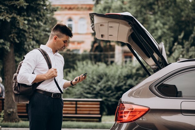 Młody przystojny biznesowy mężczyzna stojący samochodem z torbą podróżną
