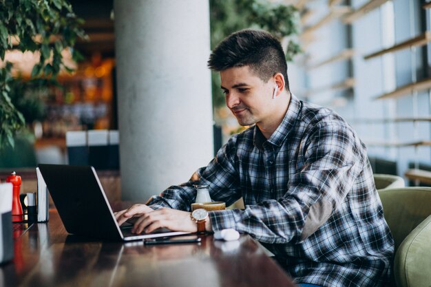 Młody przystojny biznesowy mężczyzna używa laptop w kawiarni