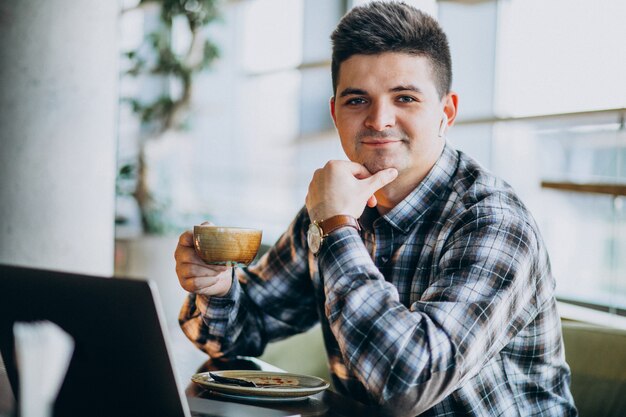 Młody przystojny biznesowy mężczyzna używa laptop w kawiarni