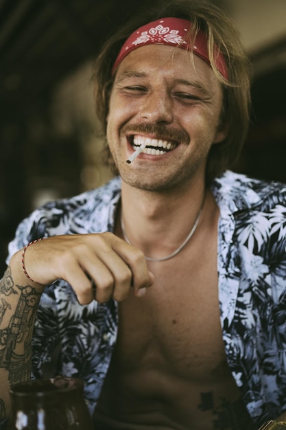 Młody przystojny hipis w czerwonej bandanie z nagim torsem zwija papierosa w kawiarni na Bali.