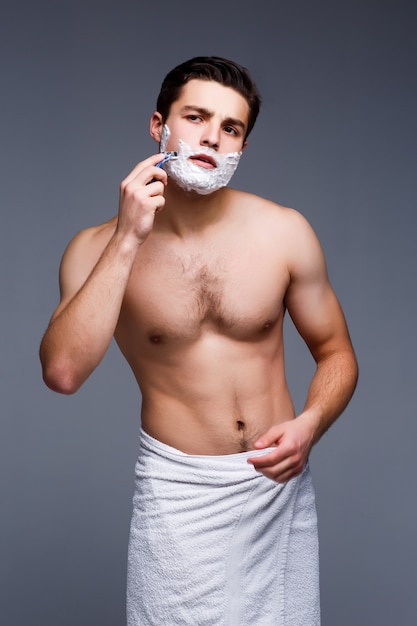 Młody przystojny mężczyzna goli się rano, pozostając na szarej ścianie